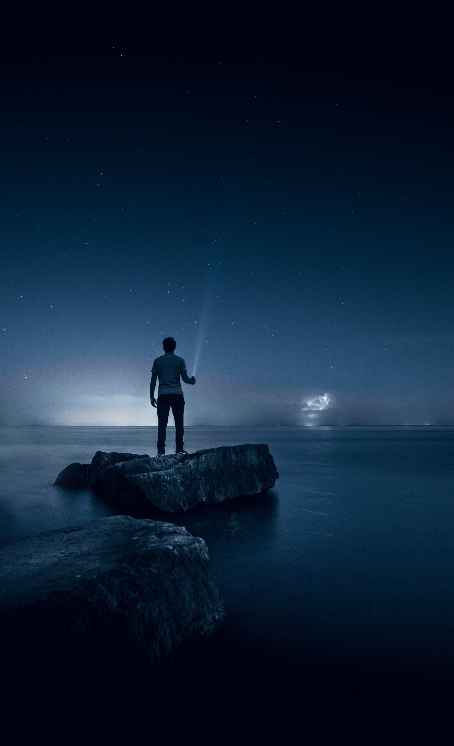 man holding flashlight, standing in boat on water at night